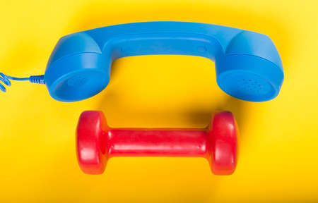 Telephone receiver and one dumbbell on yellow background