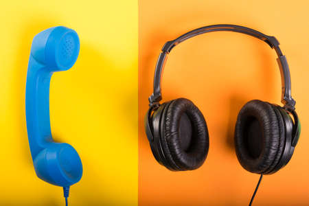 Telephone receiver and one pair of headphones on yellow and orange background