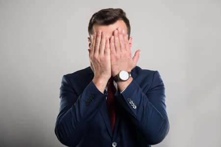 Attractive business man covering eyes like blind gesture on gray backgroundの写真素材