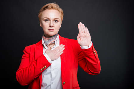 Portrait of attractive business woman making oath gesture on black background with copyspace advertising areaの写真素材