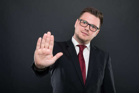 Portrait of business man wearing black suit showing stop gesture on black backgroundの写真素材