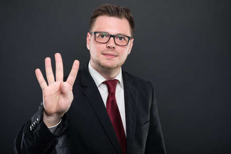 Portrait of business man wearing black suit showing number four on black background with copyspace advertising areaの写真素材