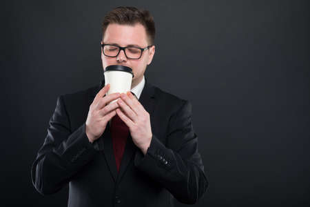 Portrait of business man smelling cup of takeaway coffee on black background with copypsace...