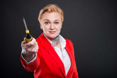 Selective focus of attractive business woman holding screwdriver looking confused on black...