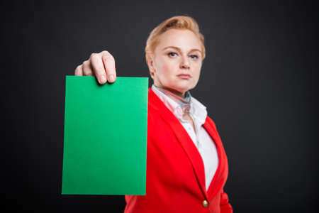 Selective focus of attractive business woman showing green cardboard on black background with...