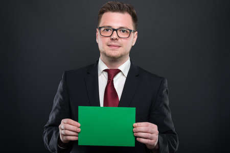 Portrait of business man holding green cardboard on black background with copyspace advertising area