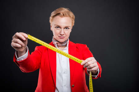 Portrait of attractive business woman holding measuring tape like slimming concept on black background with copyspace advertising areaの写真素材