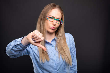 Business lady wearing blue glasses showing thumb down or dislike gesture on black background with copyspace advertising areaの写真素材