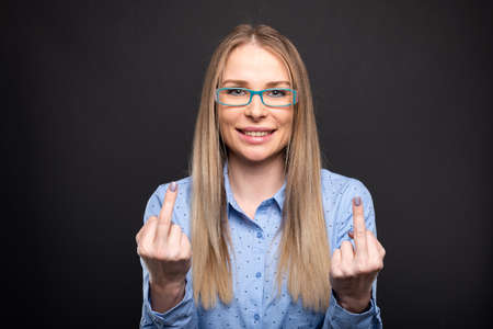 Business lady wearing blue glasses showing double obscene gesture and smiling on black background with copyspace advertising areaの写真素材