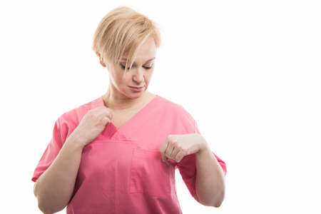 Attractive female nurse wearing pink scrubs arranging shirt isolated on white background with copyspace advertising areaの写真素材