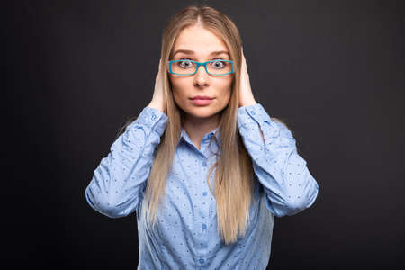 Business lady wearing blue glasses covering ears like deaf gesture on black backgroundの写真素材