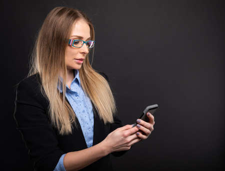 Business lady wearing blue glasses holding smartphone on black background with copyspace advertising areaの写真素材
