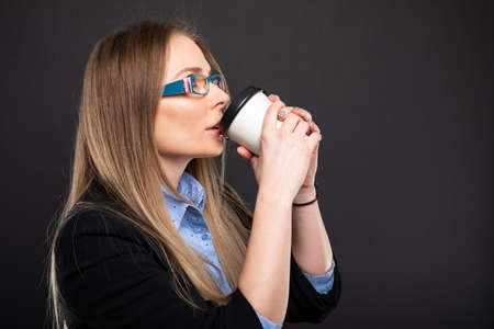 Business lady wearing blue glasses drinking coffee to go on black background with copyspace advertising areaの写真素材