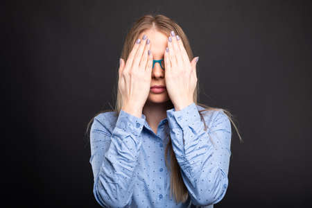 Business lady wearing blue glasses covering eyes like blind gesture on black backgroundの写真素材