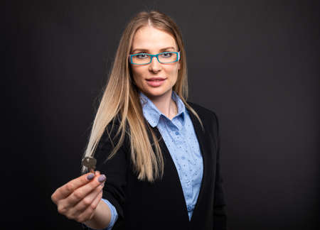 Business lady wearing blue glasses holding house key on black background with copyspace advertising areaの写真素材