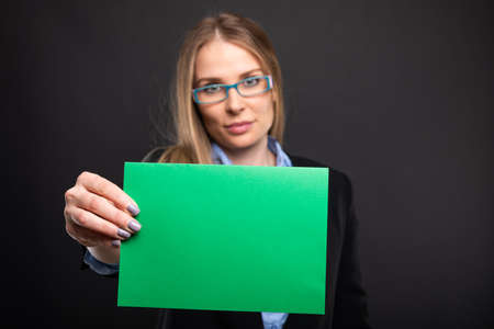 Business lady wearing blue glasses holding green cardboard on black background with copyspace advertising areaの写真素材
