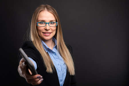 Business lady wearing blue glasses handing smartphone on black background with copyspace advertising areaの写真素材
