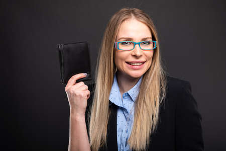 Business lady wearing blue glasses holding wallet and smiling on black background with copyspace...