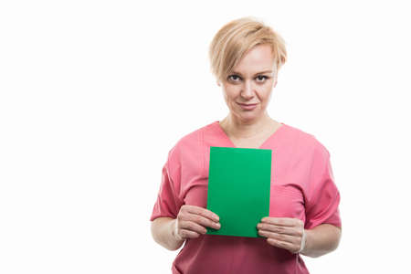 Attractive female nurse wearing pink scrubs holding green cardboard isolated on white background with copyspace advertising areaの写真素材