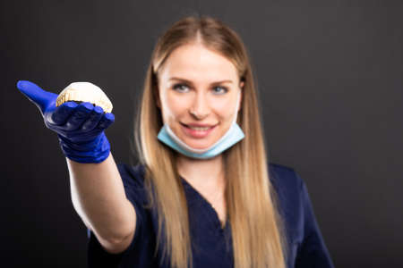 Selective focus of beautiful female dentist holding denture and smiling on black background with copyspace advertising areaの写真素材