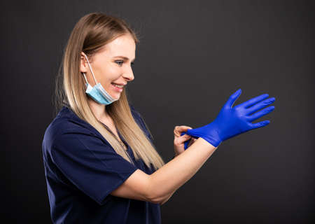 Beautiful female dentist using face mask and gloves and smiling on black background with copyspace advertising areaの写真素材