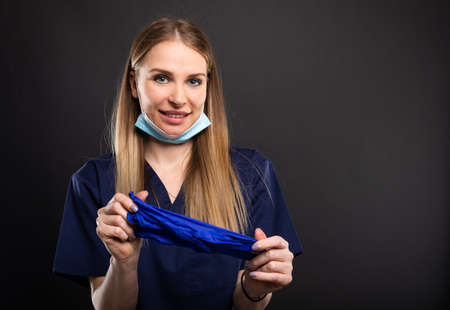 Beautiful female dentist using face mask and gloves and smiling on black background with copyspace advertising areaの写真素材