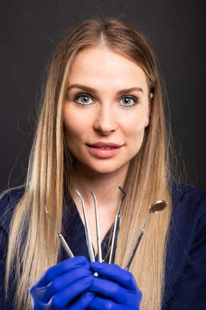 Beautiful female dentist wearing scrubs showing tools on black backgroundの写真素材