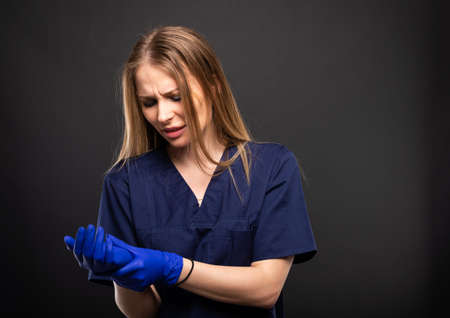 Beautiful female doctor wearing scrubs making wrist pain gesture on black background with copypsace advertising areaの写真素材