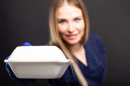 Female doctor covering nose from bad smelling lunch box on black background