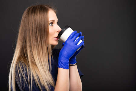 Beautiful female doctor wearing scrubs showing coffee cup on black background with copypsace advertising areaの写真素材