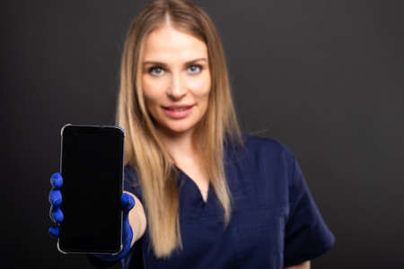 Selective focus of female doctor showing smartphone on black background with copypsace advertising areaの写真素材