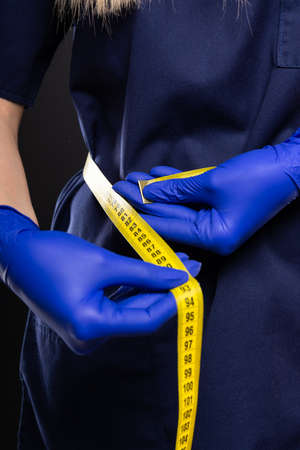 Close-up of female doctor making measuring herself with tape on black backgroundの写真素材