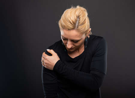 Portrait of gym female trainer holding shoulder like hurting on black background