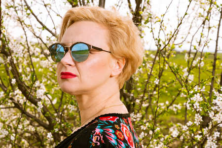 Portrait of fashionable blonde woman posing wearing shades outside on countryside background with...
