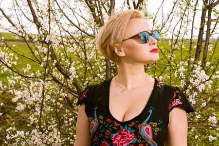 Portrait of fashionable blonde woman posing wearing shades outside on countryside background with copypsace advertising areaの写真素材