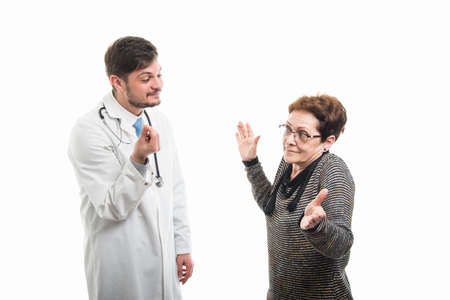 Male doctor making money gesture to female senior patient like payment concept isolated on white backgroundの写真素材