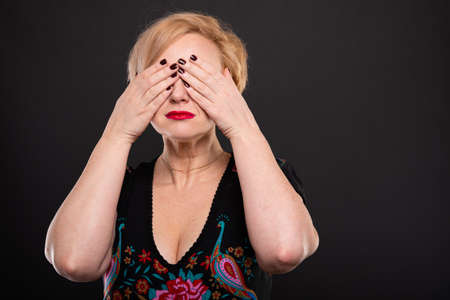 Portrait of cool fashionable woman posing covering eyes like deaf concept on black background with copypsace advertising areaの写真素材