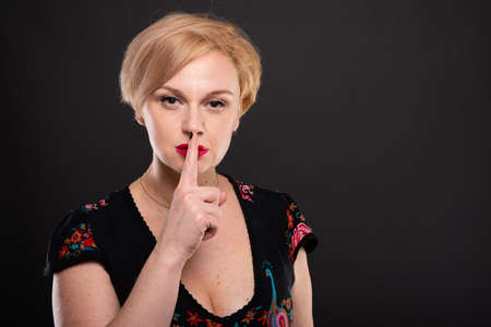 Portrait of cool fashionable woman showing silent gesture on black background with copypsace...