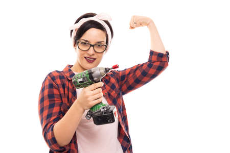Portrait of young pretty pin-up girl wearing glasses holding drill isolated on white background with...
