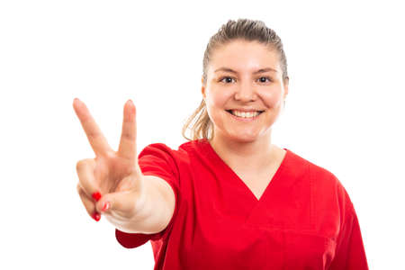 Portrait of young medical nurse wearing red scrub showing peace sign isolated on white background with copyspace advertising areaの写真素材