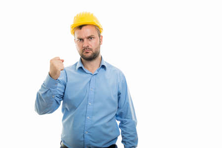 Portrait of young architect with yellow helmet showing angry fist gesture isolated on white background with copyspace advertising areaの写真素材