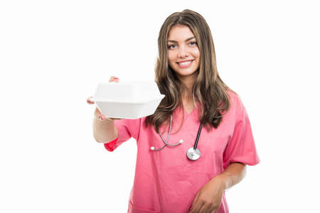 Portrait of beautiful young doctor handing lunch box isolated on white background with copy space...