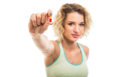 Selective focus of beautiful young fit girl showing one pill isolated on white background with copy space advertising areaの写真素材