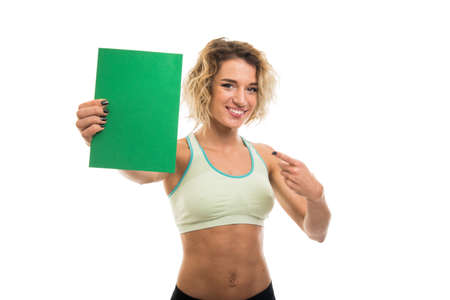 Portrait of beautiful young fit girl pointing green cardboard isolated on white background with copy space advertising areaの写真素材