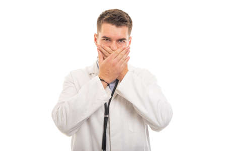 Portrait of young handsome doctor covering mouth like mute concept isolated on white background
