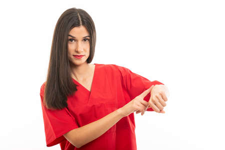 Portrait of beautiful young nurse wearing scrubs showing time gesture isolated on white background with advertising areaの写真素材