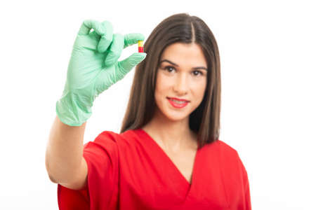 Selective focus of beautiful nurse wearing scrubs showing one pill isolated on white background with copy space advertising areaの写真素材