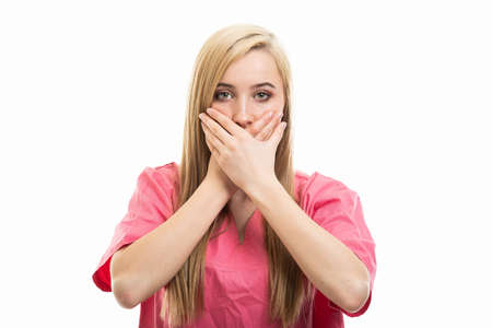Portrait of young female nurse covering mouth like mute gesture isolated on white background