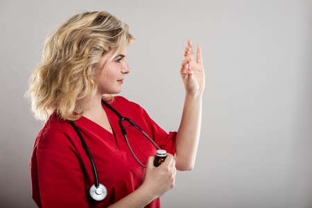 Portrait of female nurse wearing red scrub holding one pill on studio gray background with copy space advertising areaの写真素材