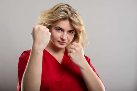 Portrait of female nurse wearing red scrub showing fists gesture on studio gray background with copy...